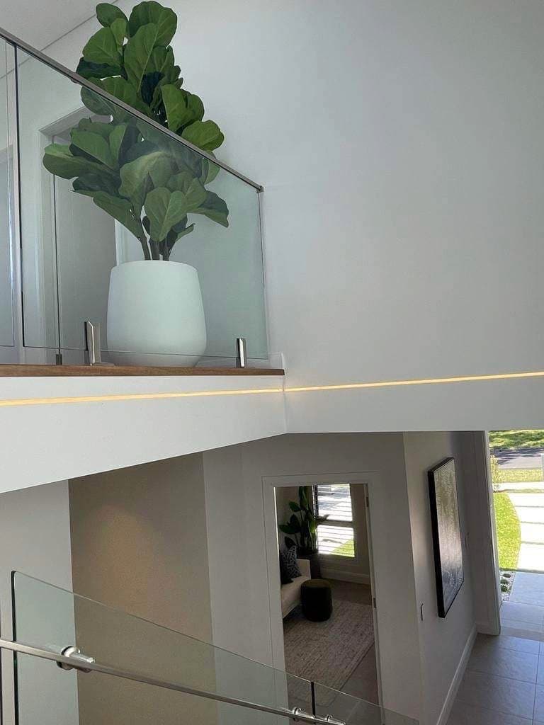 Strip lighting along the edge of a landing beside a glass stair balustrade
