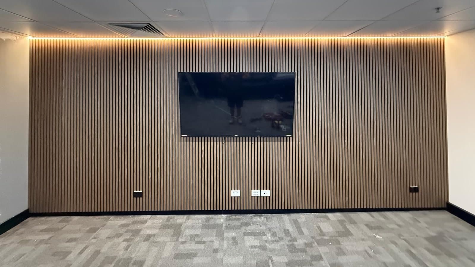 Television mounted on a timber slat wall beneath a continuous warm LED strip