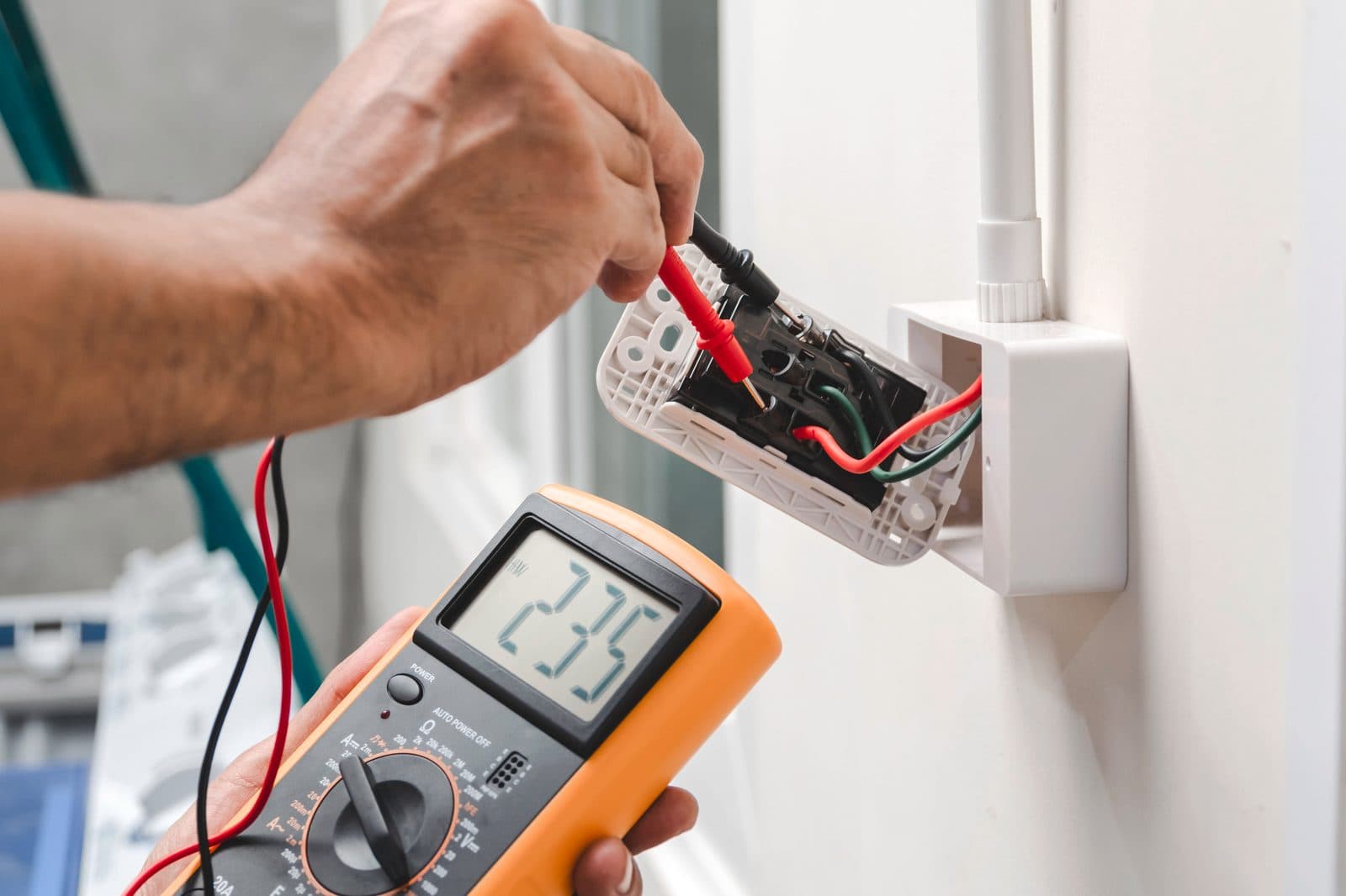 Electrician testing a wall power point with a multimeter