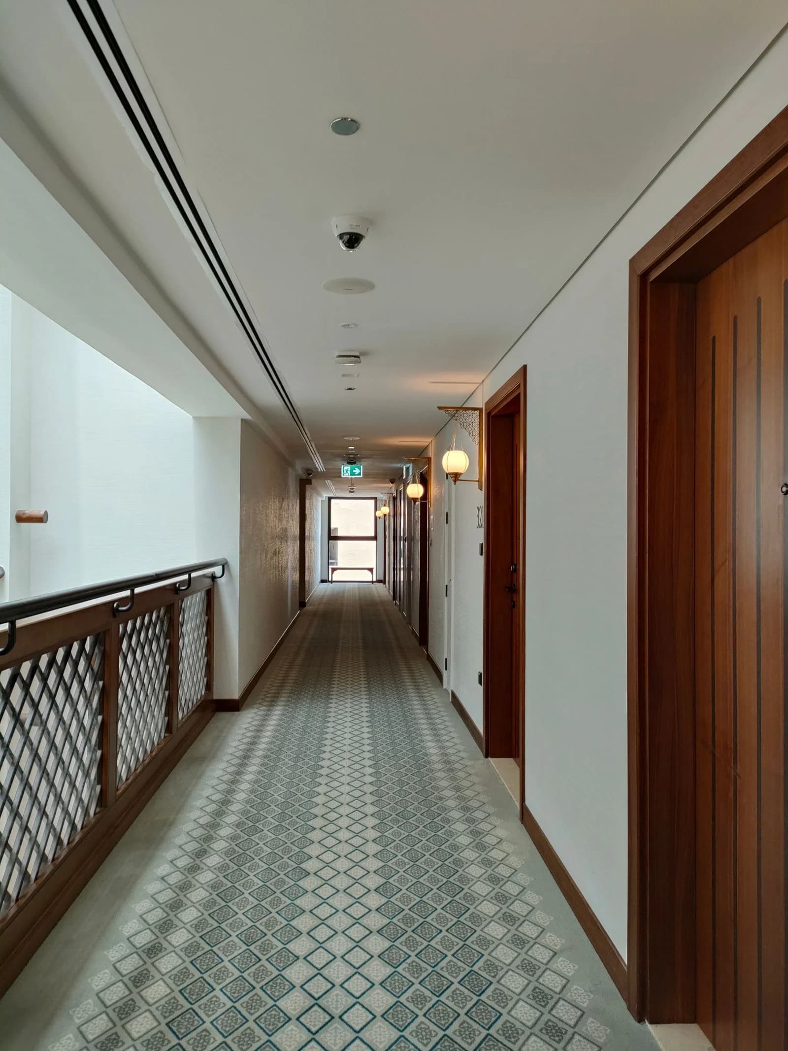Shared corridor with wall lights, ceiling safety equipment and an illuminated exit sign