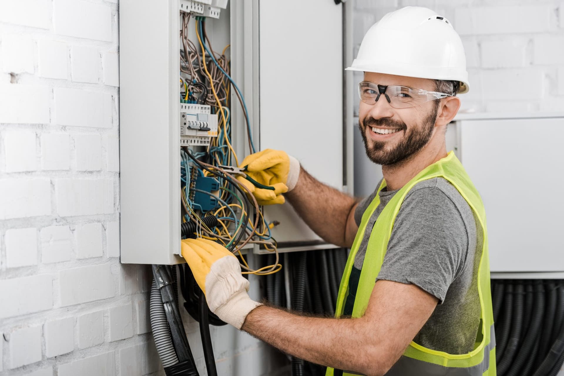 Electrician in a hard hat working on the wiring of an open electrical panel