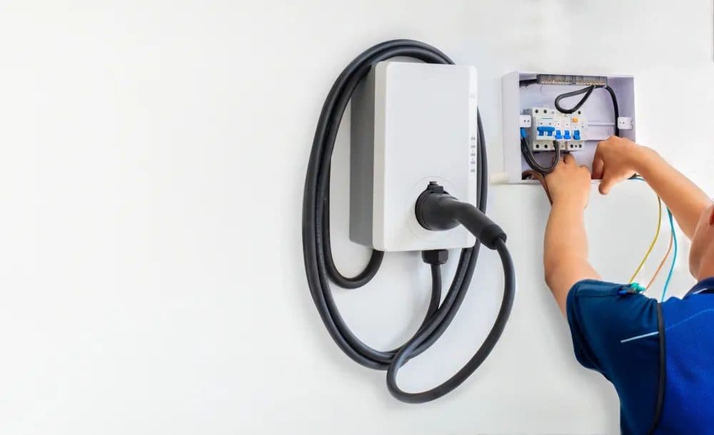 An installer working beside a wall-mounted EV charger and electrical enclosure