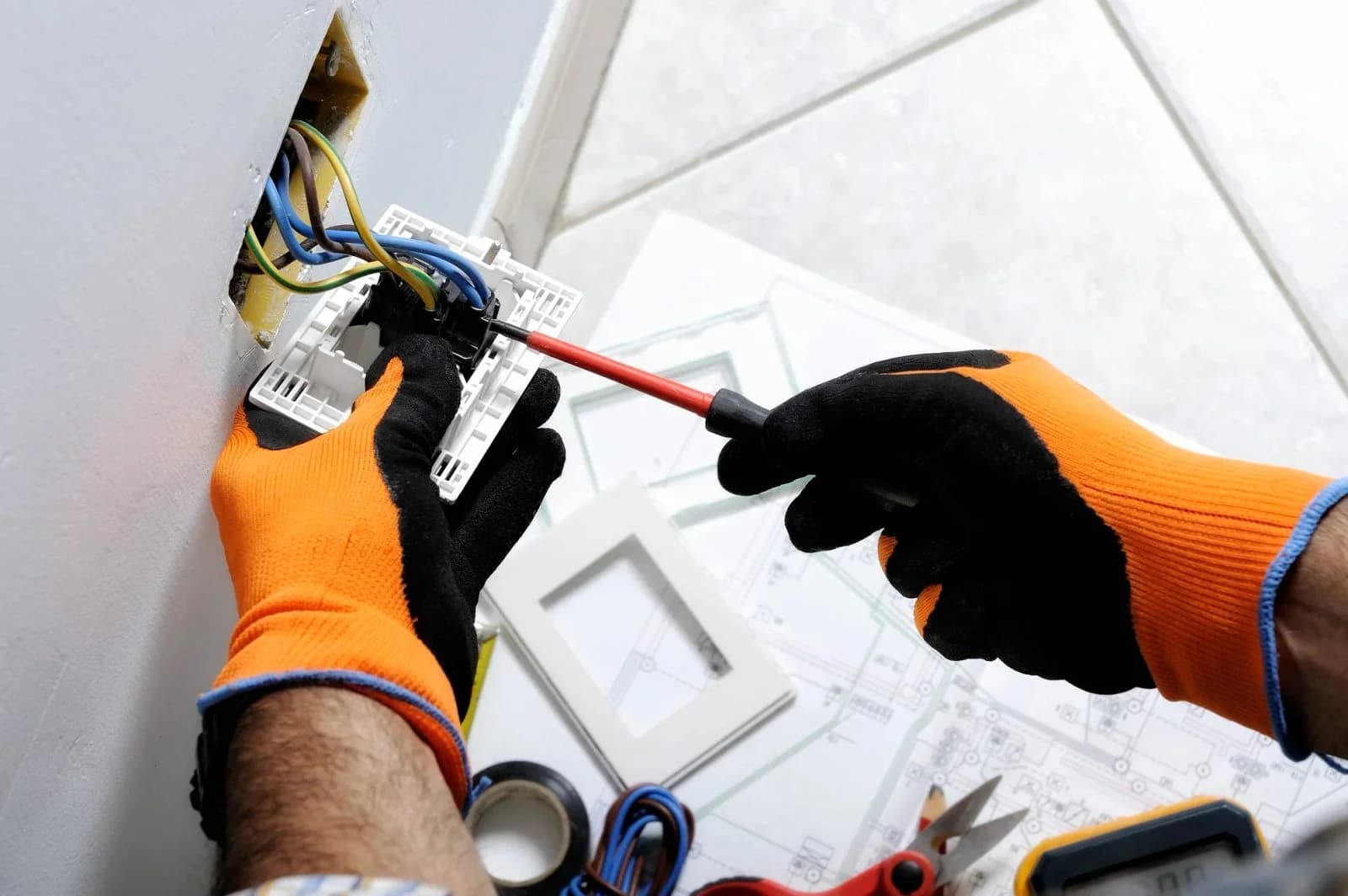Gloved hands connecting wall wiring beside an electrical plan