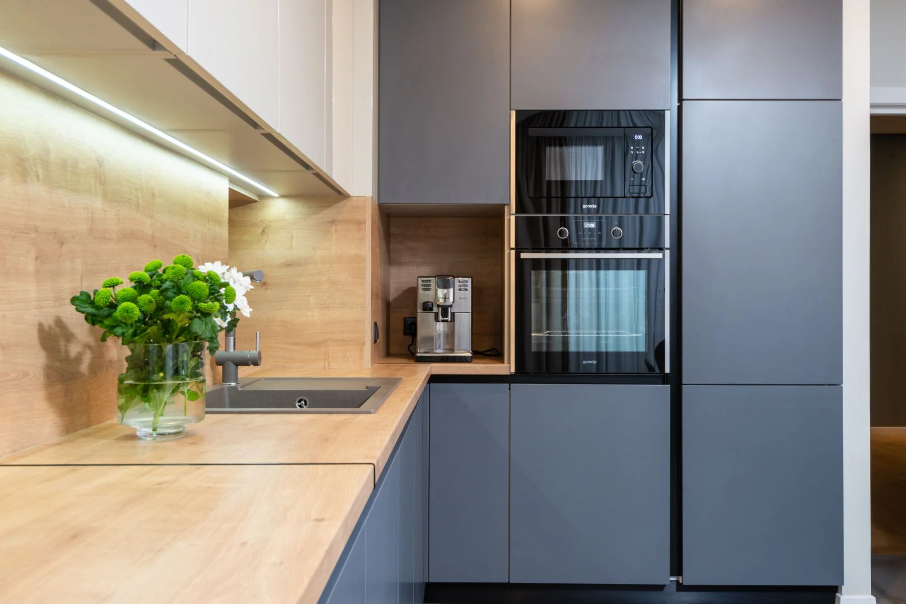 Built-in electric oven and microwave beside a timber benchtop in a modern grey kitchen
