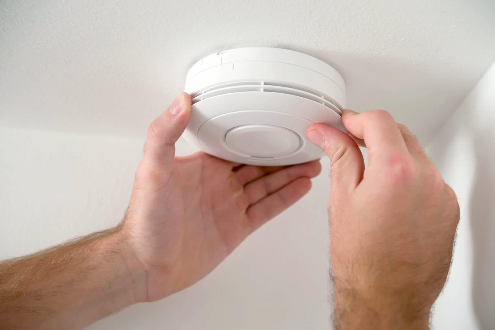 Hands fitting a smoke alarm to a white ceiling