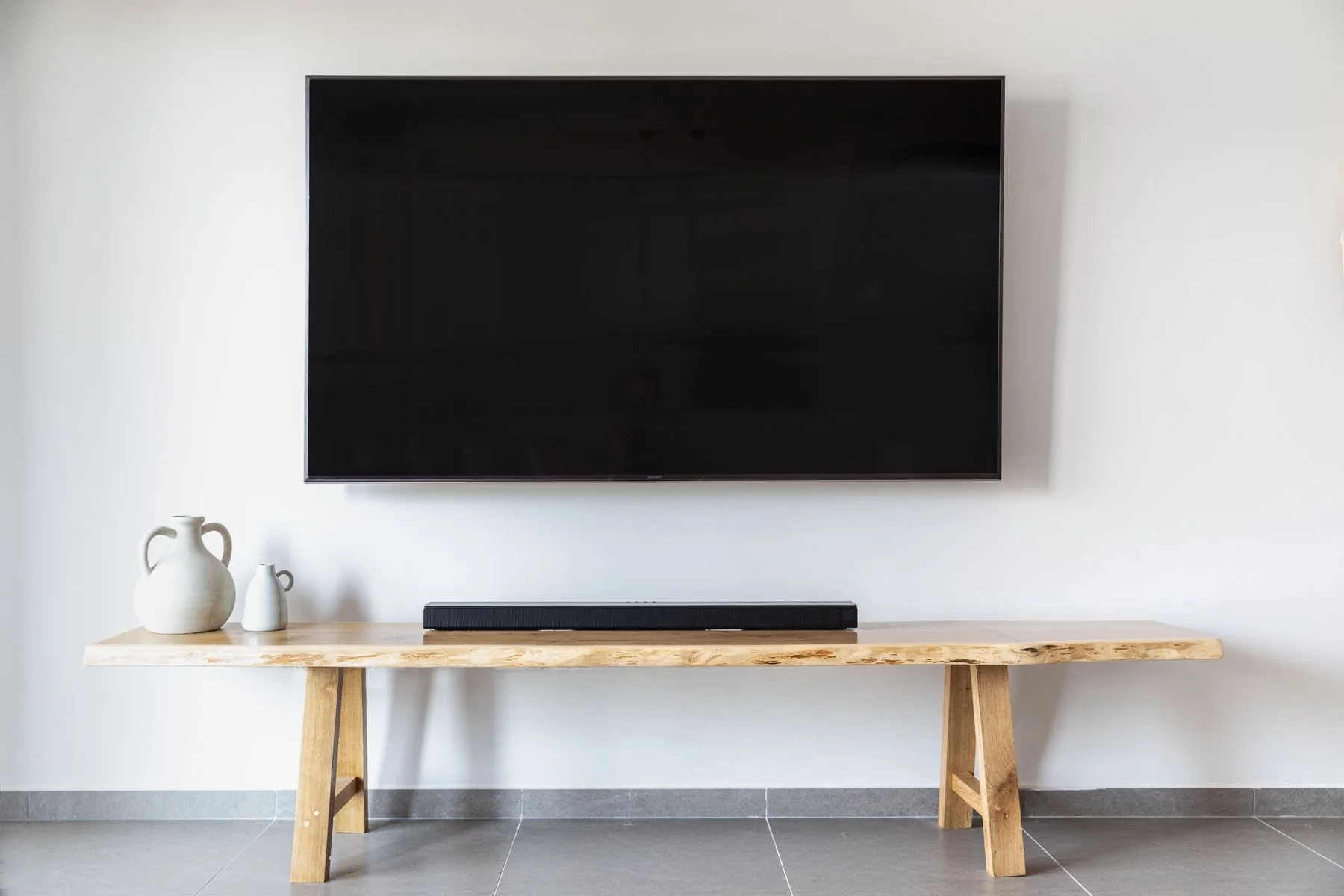 Wall-mounted television above a timber console and soundbar, with no visible trailing cables